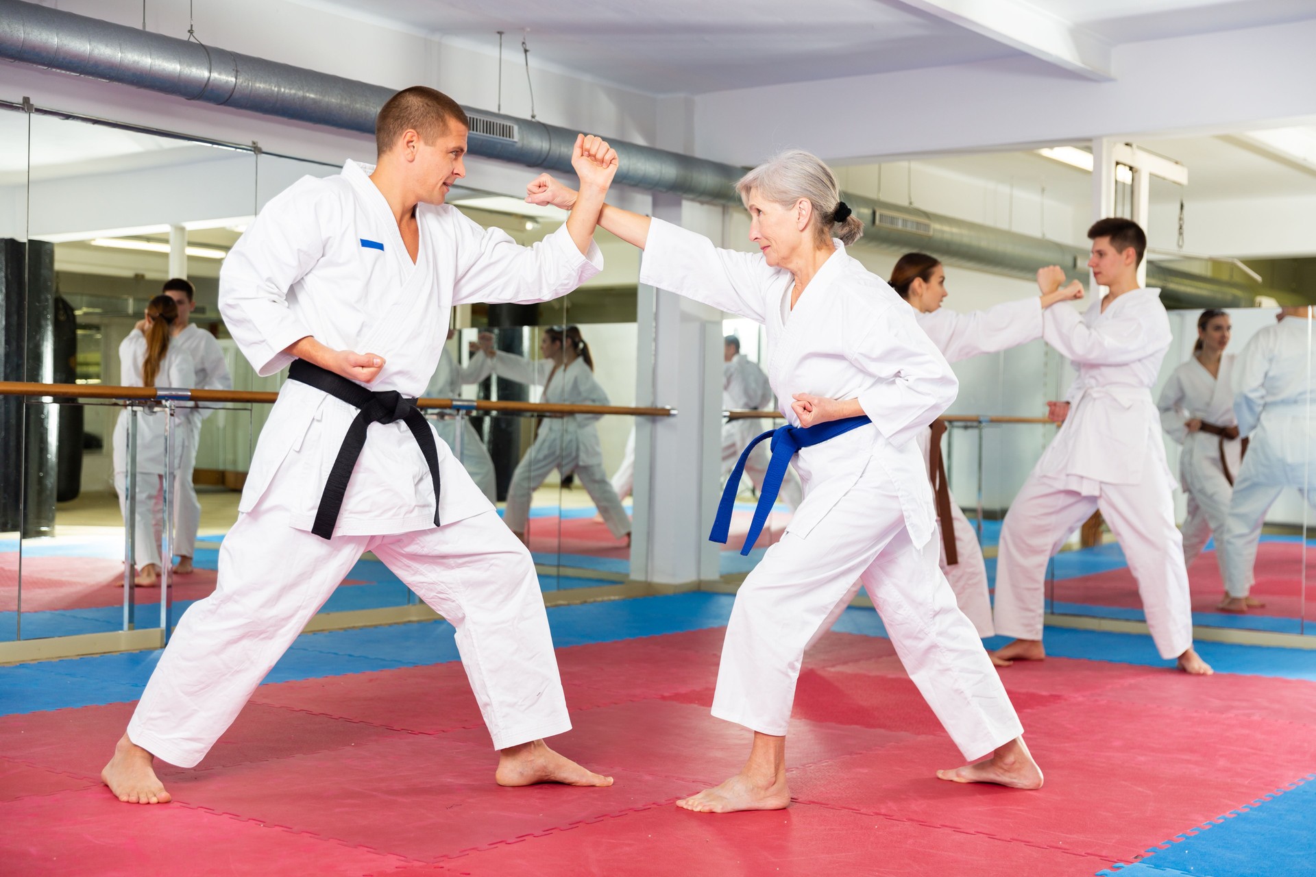 Aged woman in white kimono sparring with male opponent in gym
